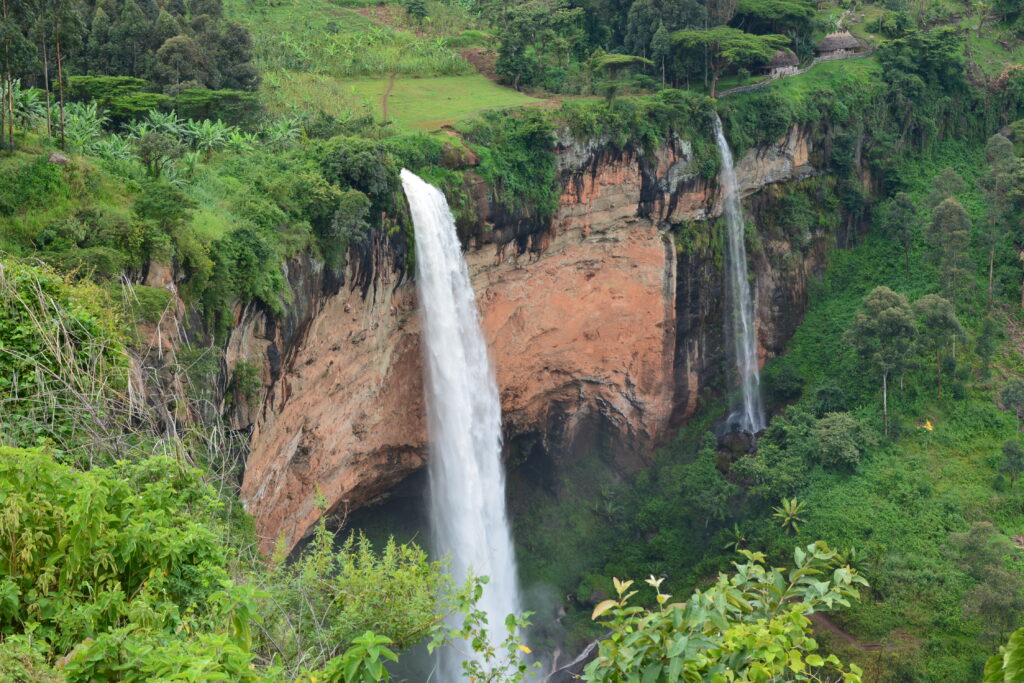 view of Sipi Falls cascading down lush green cliffs surrounded by vibrant  vegetation with mist rising from the bottom of the waterfalls